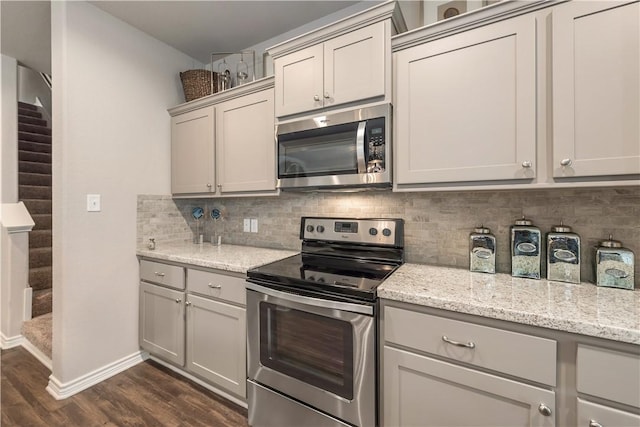 kitchen featuring light stone countertops, dark wood-style floors, baseboards, appliances with stainless steel finishes, and backsplash