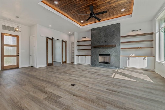 unfurnished living room featuring a tiled fireplace, wood ceiling, light hardwood / wood-style floors, a raised ceiling, and a barn door