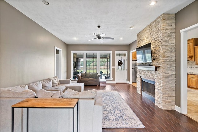 living area featuring a textured ceiling, dark wood-type flooring, visible vents, a fireplace, and a ceiling fan