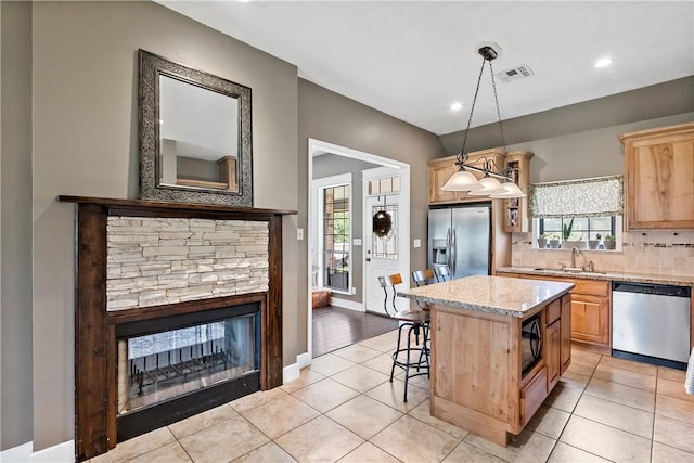 kitchen with light tile patterned floors, a center island, a sink, appliances with stainless steel finishes, and light stone counters