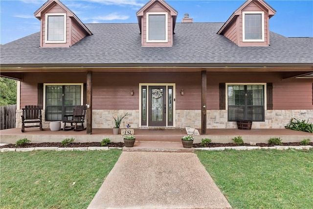 view of front of property featuring covered porch, a shingled roof, stone siding, and a front yard