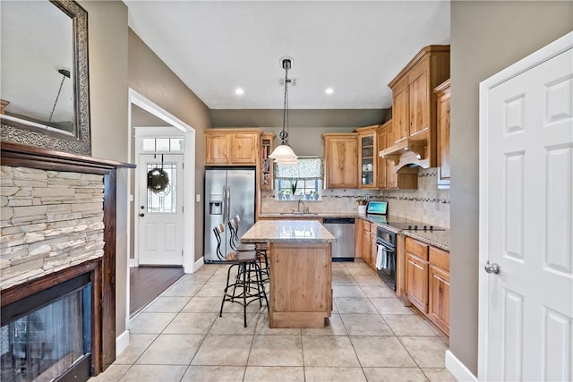 kitchen with a center island, a sink, black appliances, backsplash, and light stone counters