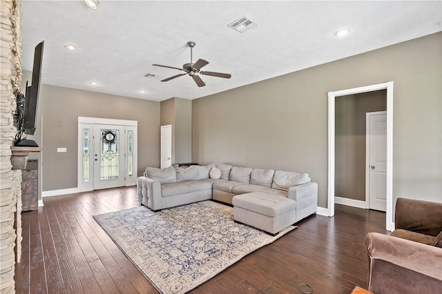 living room with visible vents, ceiling fan, dark wood-style floors, baseboards, and a stone fireplace