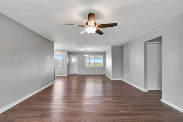 unfurnished living room with dark wood-type flooring and ceiling fan with notable chandelier