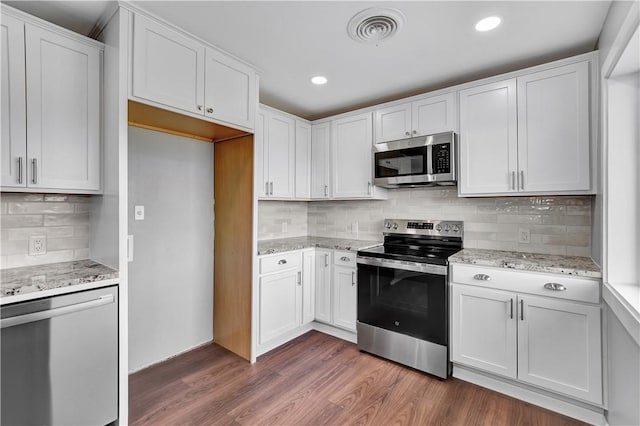 kitchen with backsplash, stainless steel appliances, dark hardwood / wood-style floors, light stone counters, and white cabinets