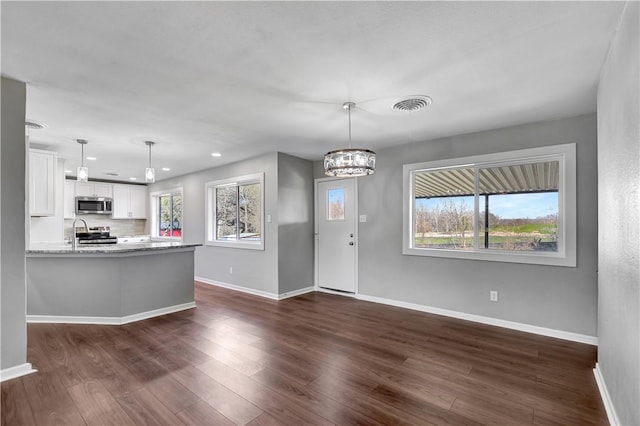 kitchen with dark wood-type flooring, white cabinetry, kitchen peninsula, stainless steel appliances, and light stone countertops