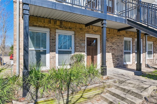 property entrance with a balcony, covered porch, and brick siding