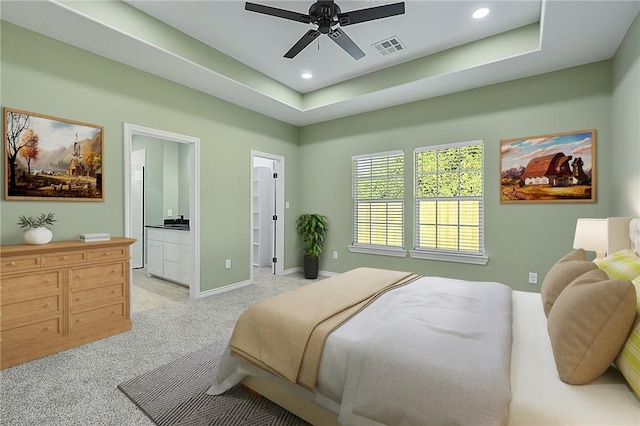 bedroom with light carpet, ensuite bathroom, ceiling fan, and a tray ceiling