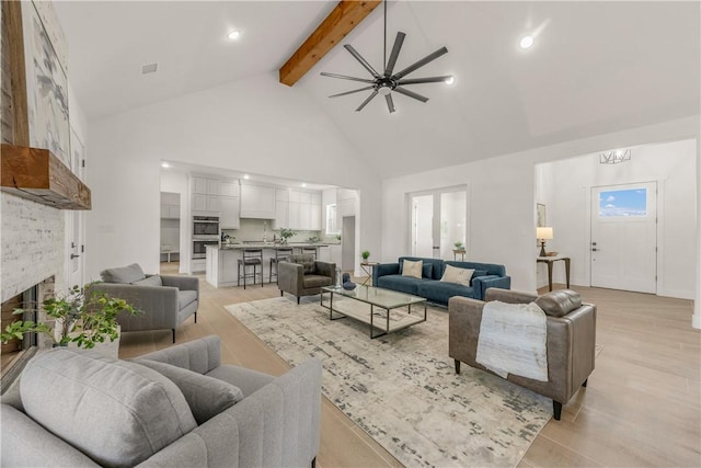 living room featuring high vaulted ceiling, a stone fireplace, ceiling fan, light wood-type flooring, and beam ceiling
