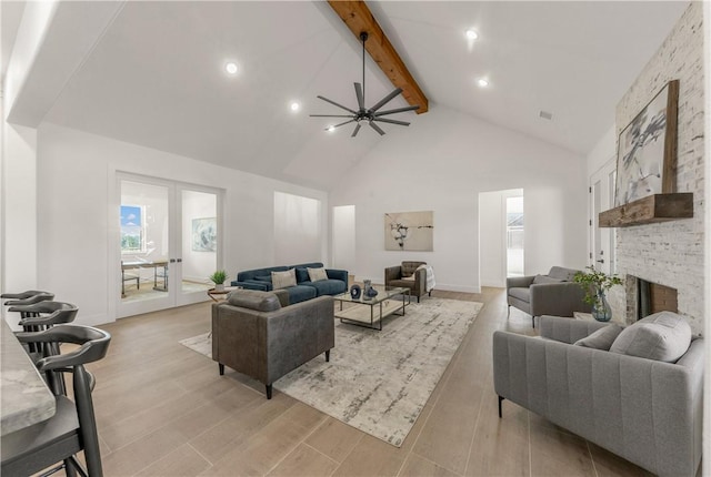 living room with ceiling fan, beam ceiling, high vaulted ceiling, light hardwood / wood-style flooring, and a stone fireplace
