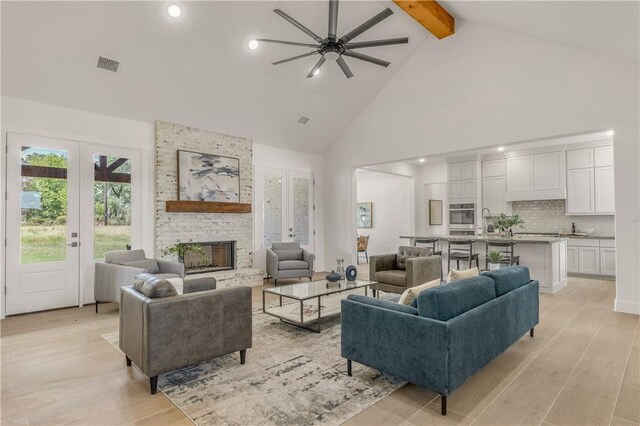 living room featuring beamed ceiling, light wood-type flooring, high vaulted ceiling, and ceiling fan