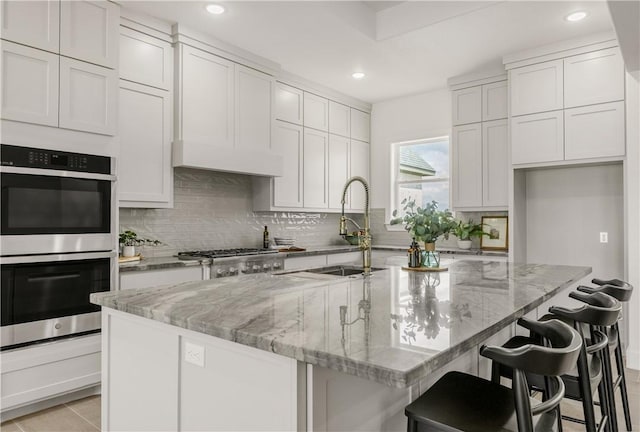 kitchen with a kitchen breakfast bar, light stone counters, a center island with sink, and stainless steel appliances