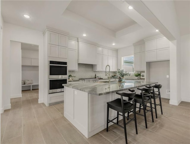 kitchen with light stone counters, stainless steel appliances, a spacious island, sink, and white cabinets