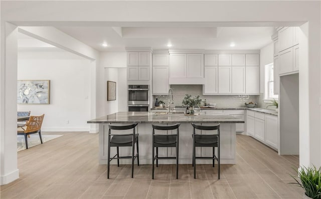 kitchen featuring stone countertops, light wood-type flooring, a kitchen island with sink, and a breakfast bar area