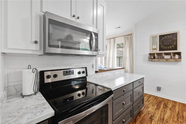 6866 Wooded Dr, College Station, TX 77845 - kitchen featuring stainless steel appliances, wood finished floors, light stone counters, white cabinets, and wooden walls