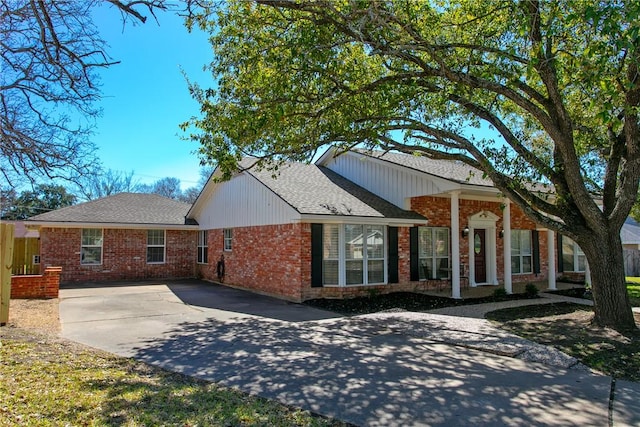 view of front of home with brick siding, driveway, and roof with shingles