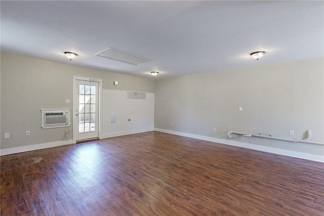 unfurnished living room featuring attic access, baseboards, wood finished floors, and a wall mounted air conditioner