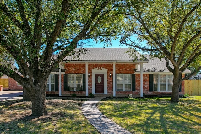 view of front facade featuring roof with shingles, fence, a front lawn, and brick siding