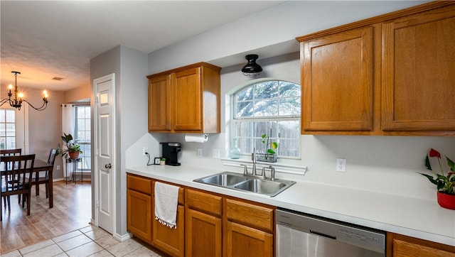 kitchen with a sink, light countertops, stainless steel dishwasher, brown cabinets, and a chandelier