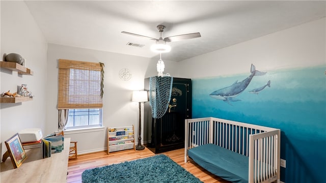 bedroom featuring visible vents, baseboards, a nursery area, and wood finished floors