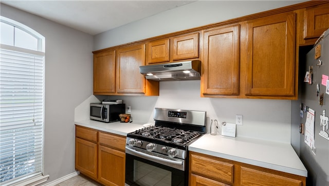 kitchen with light countertops, brown cabinetry, appliances with stainless steel finishes, and under cabinet range hood