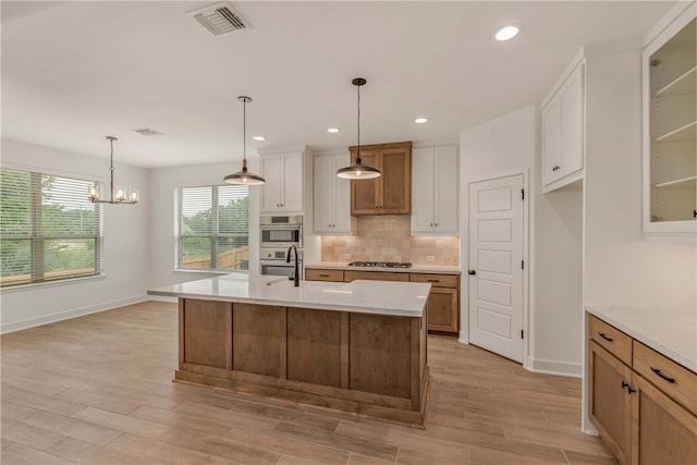 3568 Chantilly Path, Bryan, TX 77808 - kitchen featuring appliances with stainless steel finishes, decorative backsplash, light wood-type flooring, white cabinetry, and a chandelier