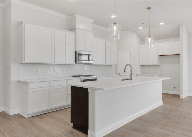 kitchen featuring a center island with sink, white cabinets, stainless steel appliances, and decorative light fixtures