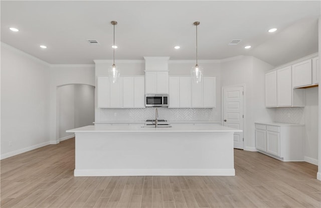 kitchen with white cabinets, light hardwood / wood-style floors, hanging light fixtures, and an island with sink