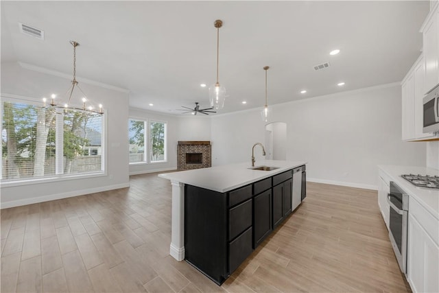 kitchen with sink, pendant lighting, a kitchen island with sink, ceiling fan with notable chandelier, and appliances with stainless steel finishes