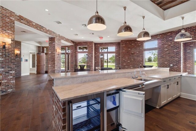 4209 Harding Ct, Bryan, TX 77802 - kitchen with brick wall, dark wood-style floors, pendant lighting, white cabinetry, and beverage cooler