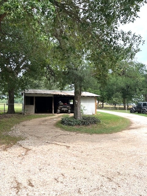 view of front facade featuring an outdoor structure, dirt driveway, fence, and a carport