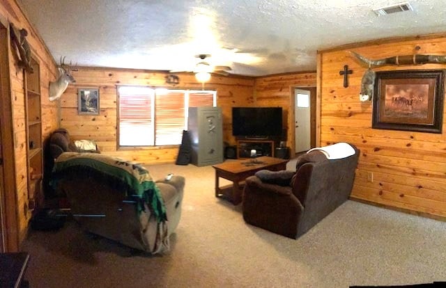 carpeted living area with visible vents, wood walls, a textured ceiling, and a ceiling fan