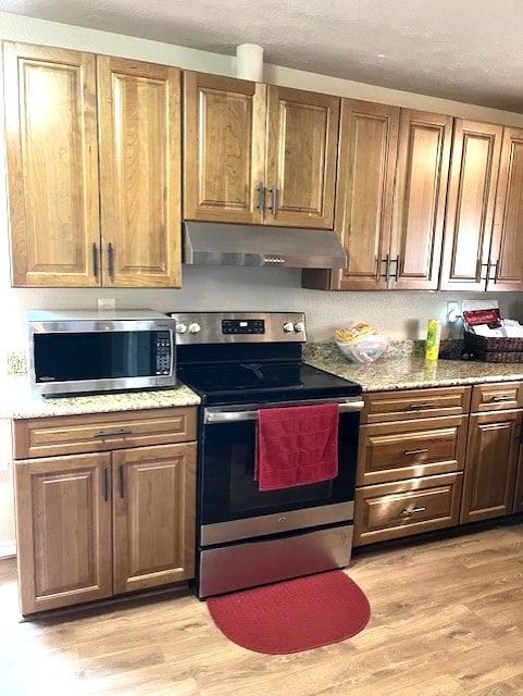 kitchen featuring under cabinet range hood, stainless steel appliances, light stone countertops, and light wood-type flooring