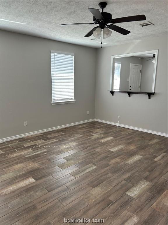 empty room with a textured ceiling, ceiling fan, a healthy amount of sunlight, and dark wood-type flooring