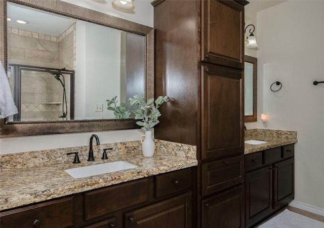 bathroom with double vanity, a stall shower, a sink, and baseboards