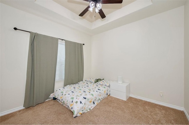 bedroom with a raised ceiling, light carpet, ceiling fan, and baseboards