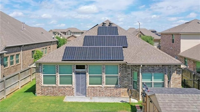 back of house featuring a yard, fence private yard, roof mounted solar panels, and brick siding