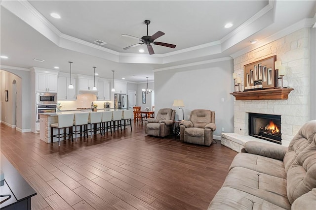 living room featuring dark wood-type flooring, a tray ceiling, arched walkways, and ceiling fan with notable chandelier