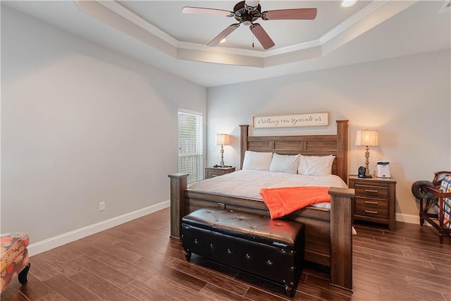 bedroom featuring ceiling fan, wood finished floors, baseboards, a raised ceiling, and crown molding