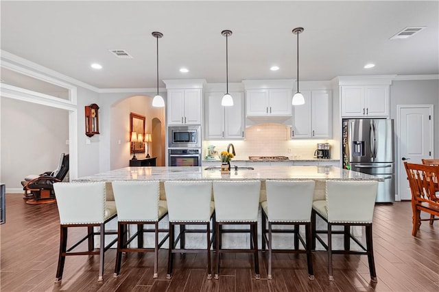 kitchen featuring arched walkways, a spacious island, visible vents, appliances with stainless steel finishes, and a sink