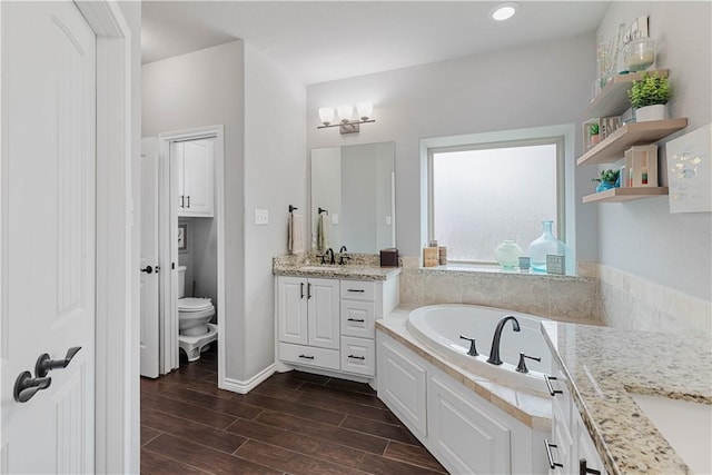 full bathroom featuring a garden tub, toilet, wood finish floors, vanity, and baseboards