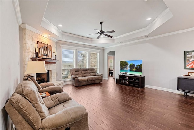 living room with dark wood-type flooring, a tray ceiling, a stone fireplace, and baseboards