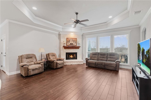 living area featuring a tray ceiling, crown molding, a fireplace, visible vents, and dark wood-type flooring