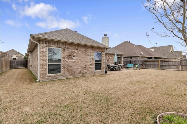 rear view of property featuring brick siding, a chimney, a shingled roof, a lawn, and a fenced backyard