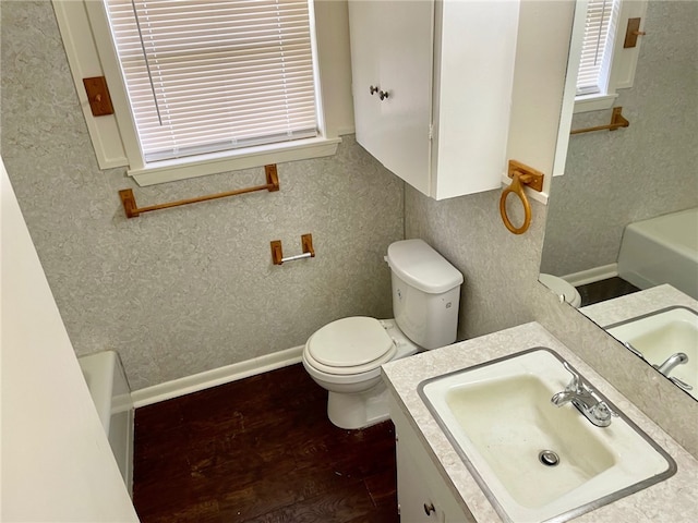 bathroom with hardwood / wood-style floors, vanity, toilet, and a tub