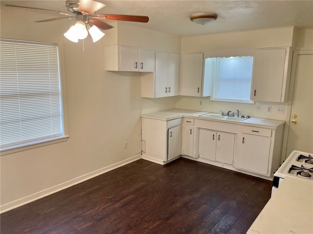 kitchen featuring dark wood-type flooring, sink, ceiling fan, white gas range, and white cabinetry