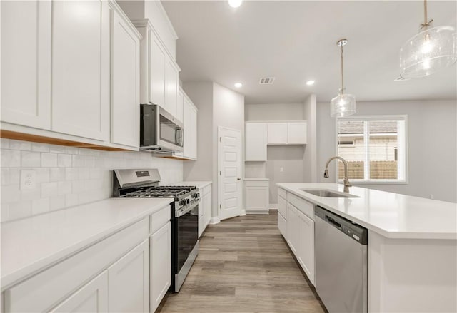 kitchen with visible vents, light wood-style flooring, a sink, decorative backsplash, and stainless steel appliances