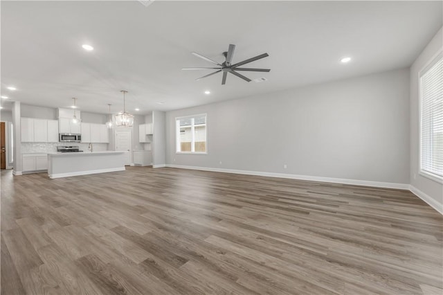 unfurnished living room with recessed lighting, ceiling fan with notable chandelier, light wood-type flooring, and baseboards