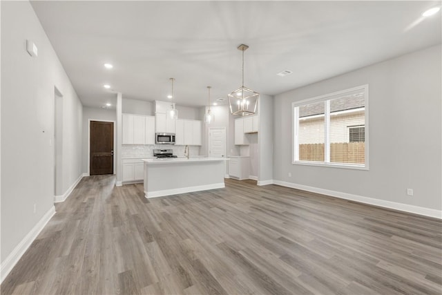 kitchen with backsplash, baseboards, light wood-style flooring, white cabinets, and stainless steel appliances