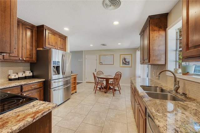 kitchen featuring sink, stainless steel fridge, decorative backsplash, and light stone countertops